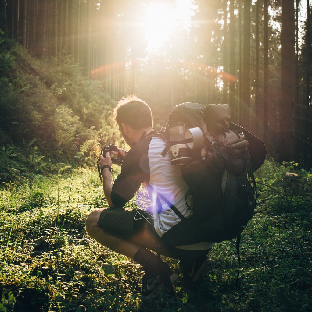 A man crouching down to get the perfect photo while backpacking through the forest