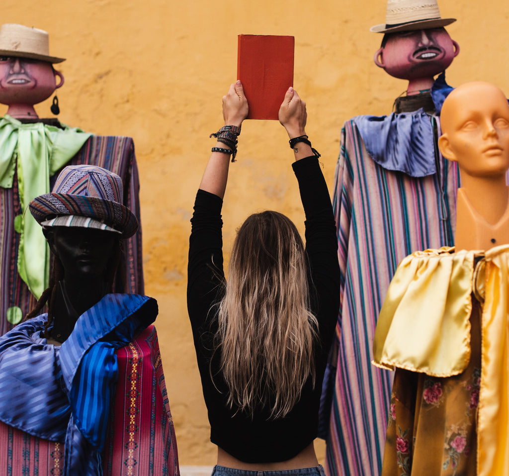 A girl holds up the Wakeful Travel Journal in the middle of four mannequins in Guatemala 
