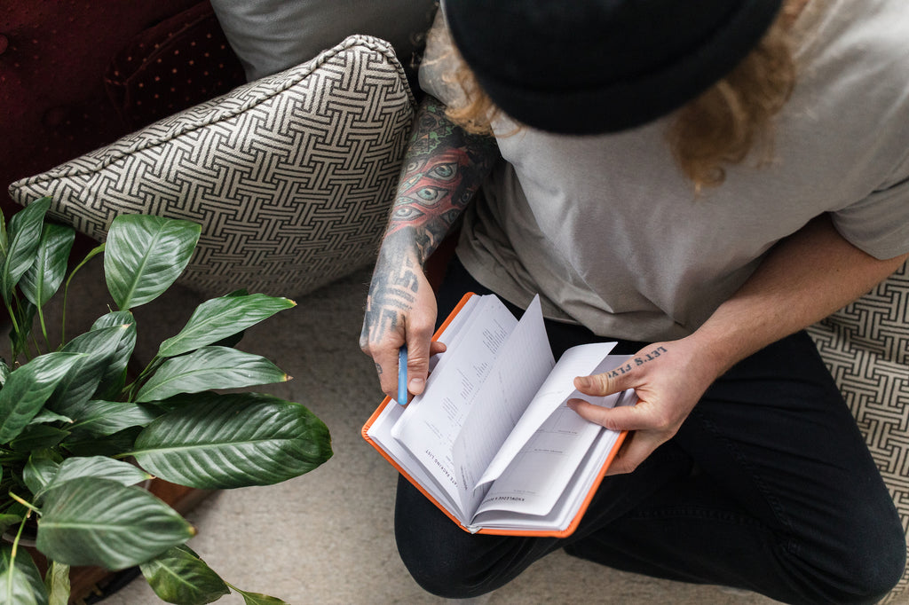 man in hat holding the mindful travel journal beside a plant